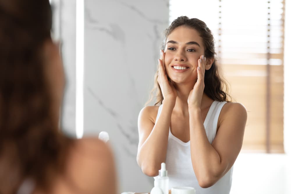 Woman smiling looking in the mirror at her skin after a chemical peel in Grapevine, TX